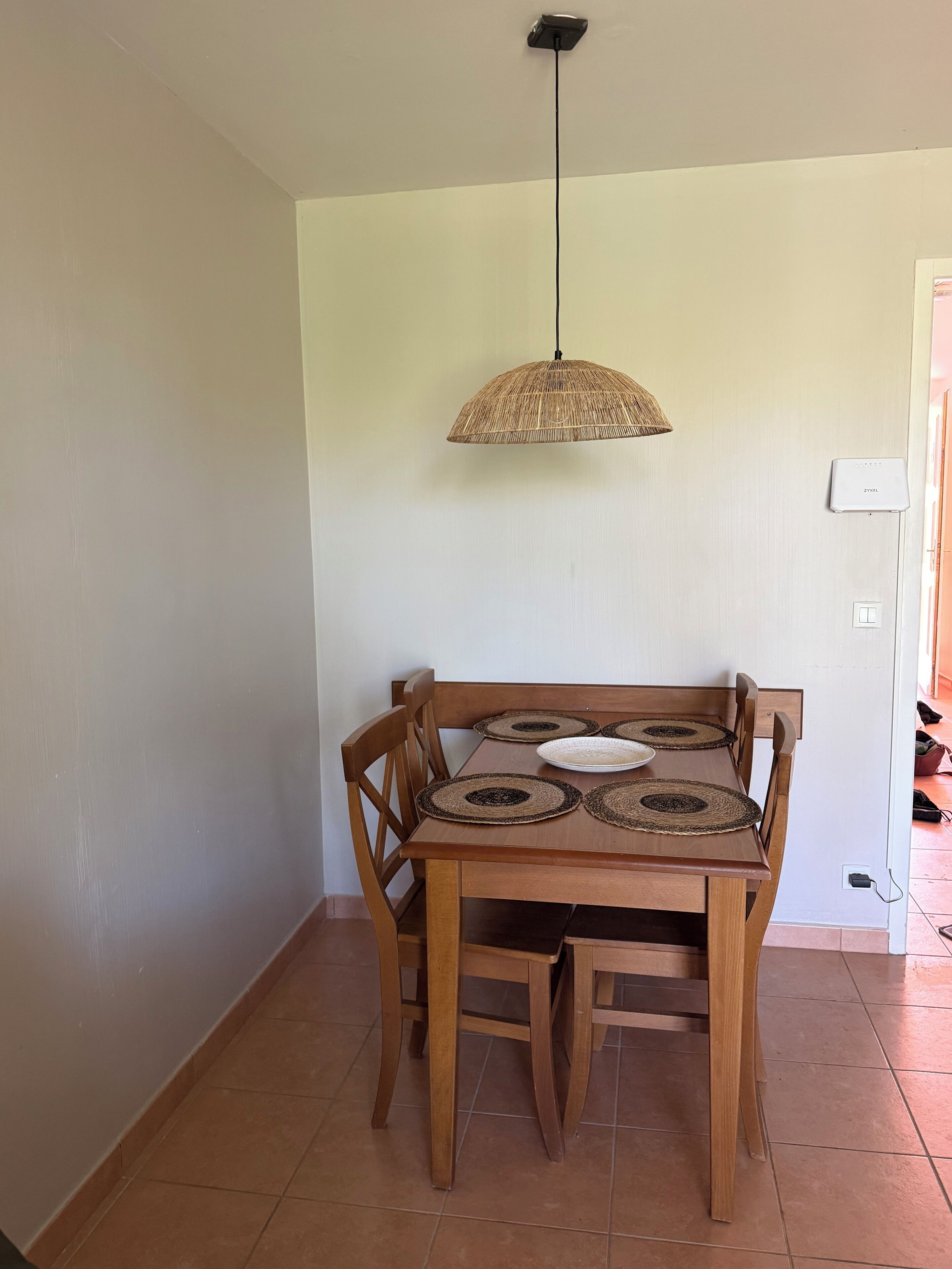 Un coin repas avec une table en bois, quatre chaises et une lampe en rotin suspendue au plafond.
