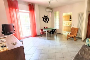 Una sala de estar con televisor, mesa de comedor, sillas y vista hacia la cocina.