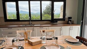 A dining area with a table set for four, a coffee machine, and a view of greenery through large windows. - Charming house in Drôme provençale - Ventoux view - 10 min from Grignan (Salles-sous-Bois)