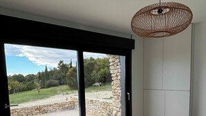 A bedroom with a large sliding glass door leading to a stone patio, a bed with a white duvet, and a woven pendant light. - Charming house in Drôme provençale - Ventoux view - 10 min from Grignan (Salles-sous-Bois)