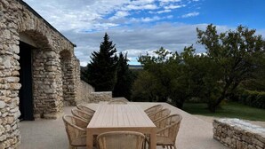 An outdoor dining area with a stone wall, a wooden table, and wicker chairs. - Charming house in Drôme provençale - Ventoux view - 10 min from Grignan (Salles-sous-Bois)