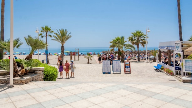 Eine Strandpromenade mit Palmen, Strandsonnenschirmen und freiem Blick auf das Meer.