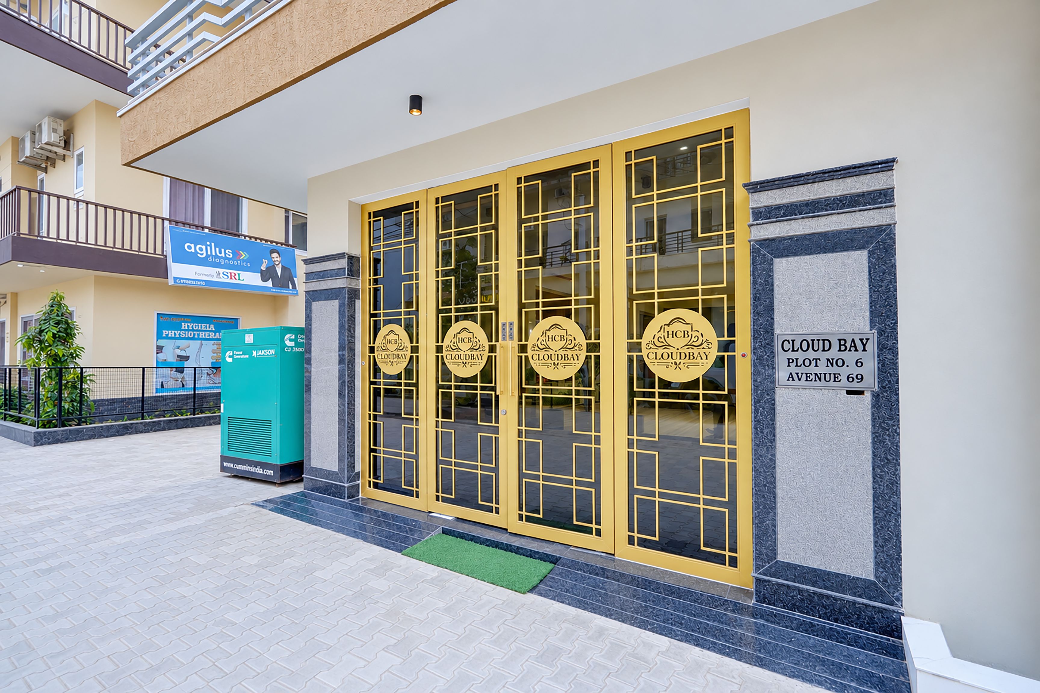 A hotel entrance with a yellow gate, a sign for 'Cloud Bay Plot No. 6 Avenue 69', and a 'Hygiene Physiotherapy' sign.