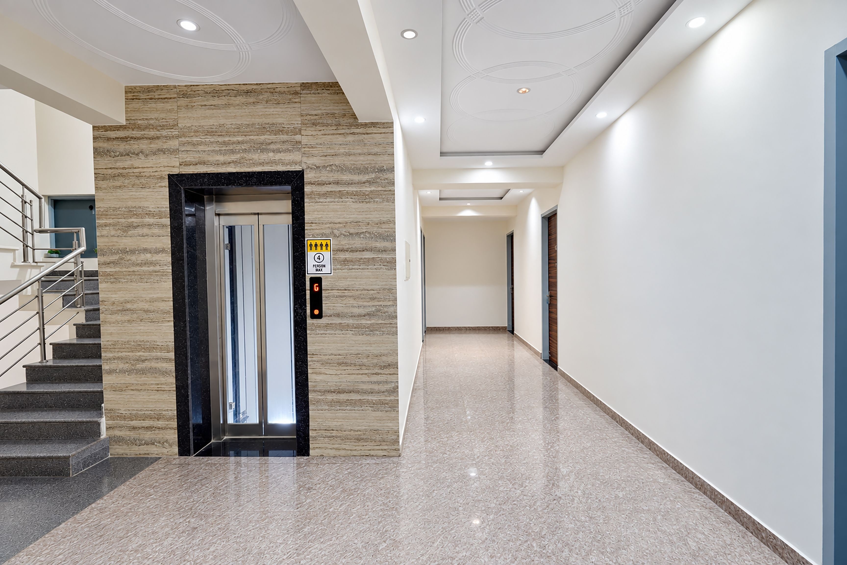 Un pasillo moderno con pared de mármol, una escalera y un panel de control digital para el ascensor.