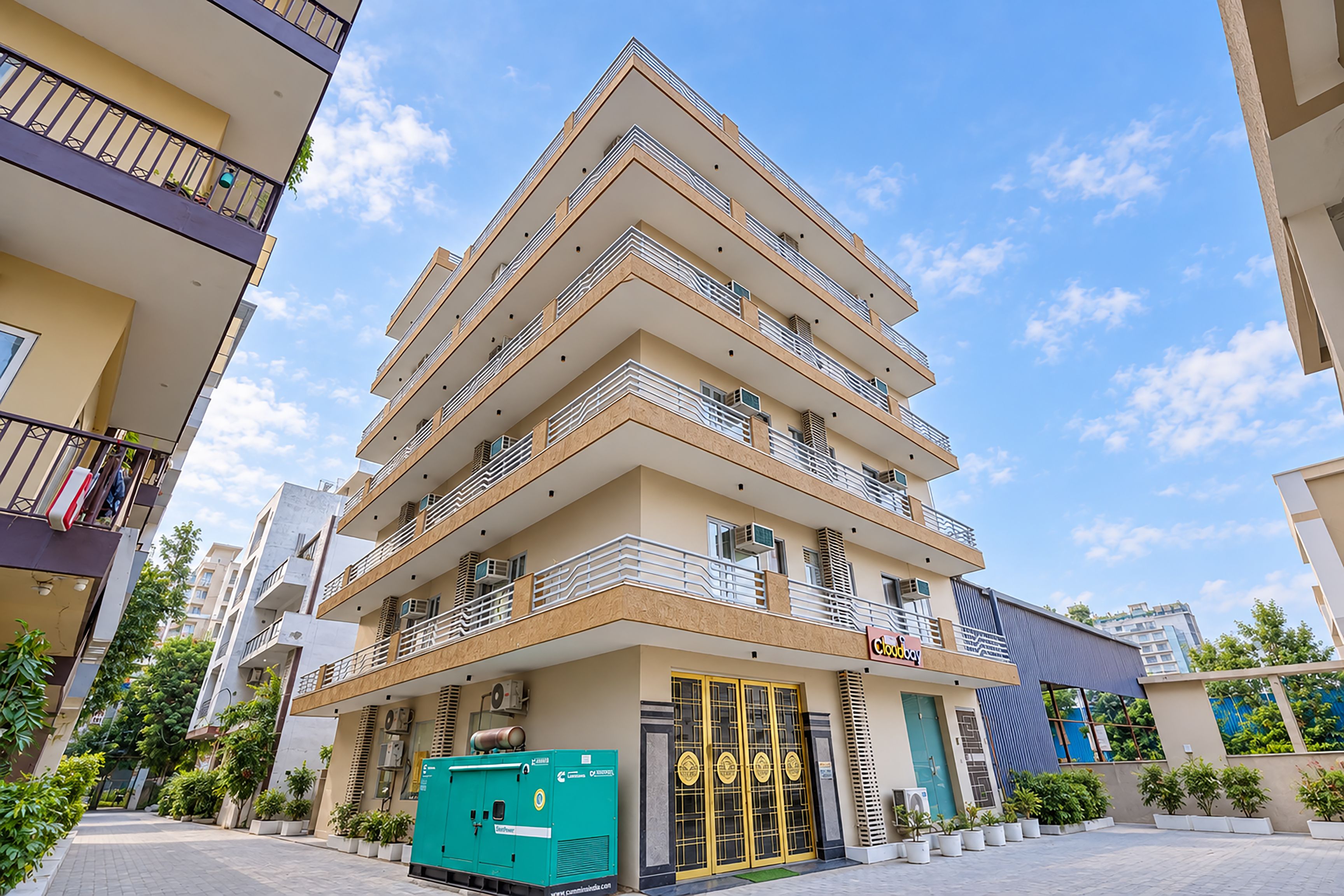 Un hôtel à plusieurs étages au design moderne, doté de balcons à chaque niveau, arborant un symbole d’énergie verte et présentant une entrée bien visible avec une porte en verre.