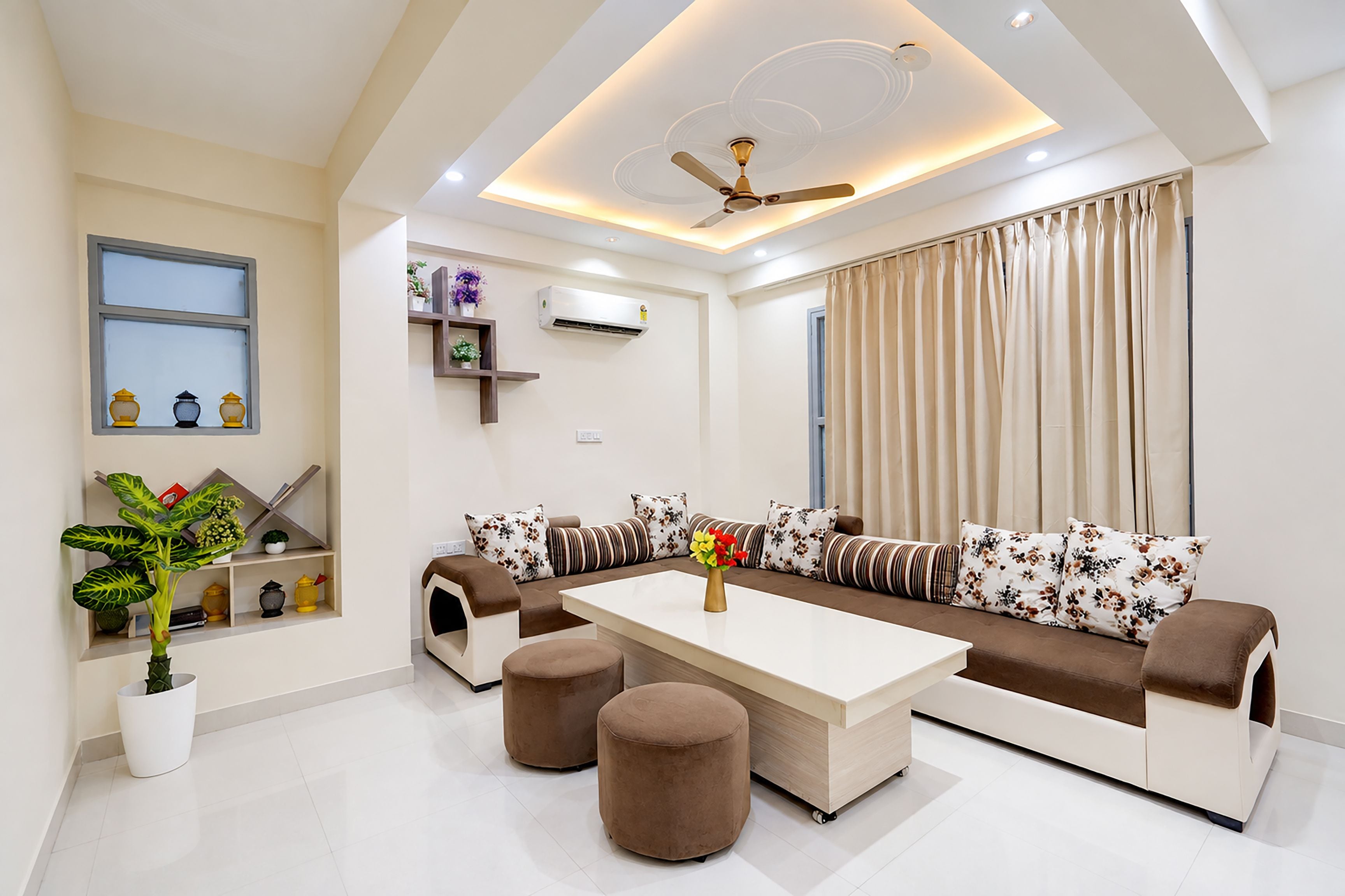 A modern living room with a sofa set, ottomans, a coffee table, a ceiling fan, and a window with curtains.