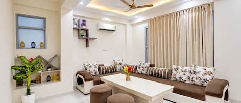 A modern living room with a sofa set, ottomans, a coffee table, a ceiling fan, and a window with curtains.
