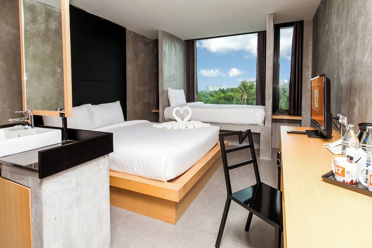 Habitación de hotel moderna con una cama grande, un escritorio con computadora, un baño con lavamanos y vistas a zonas verdes.