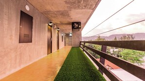 Un pasillo con césped artificial verde, puertas de madera y un balcón con vistas a la vegetación y colinas.