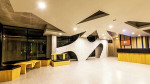 Un área de recepción moderna con un diseño arquitectónico único, que incluye una pared grande con recortes geométricos y un mostrador de recepción.
