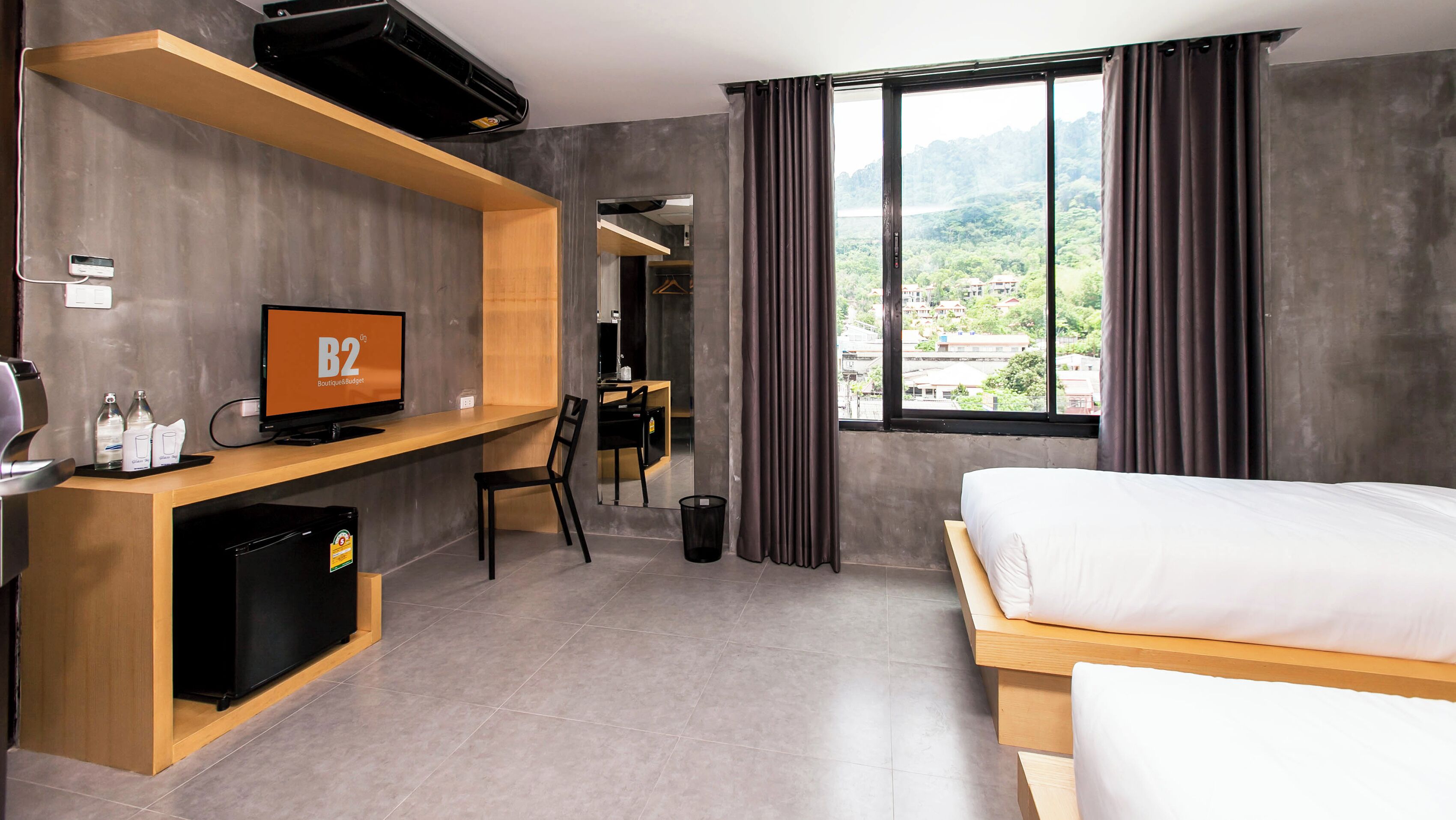A hotel room with a bed, a desk with a computer, a television, and a view of a mountainous landscape.