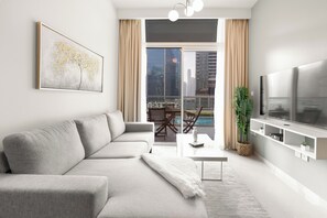 Ein modernes Wohnzimmer mit grauem Sofa, einem Flachbildfernseher, einem großen Fenster mit Stadtblick und einem Essbereich mit Tisch und Stühlen.