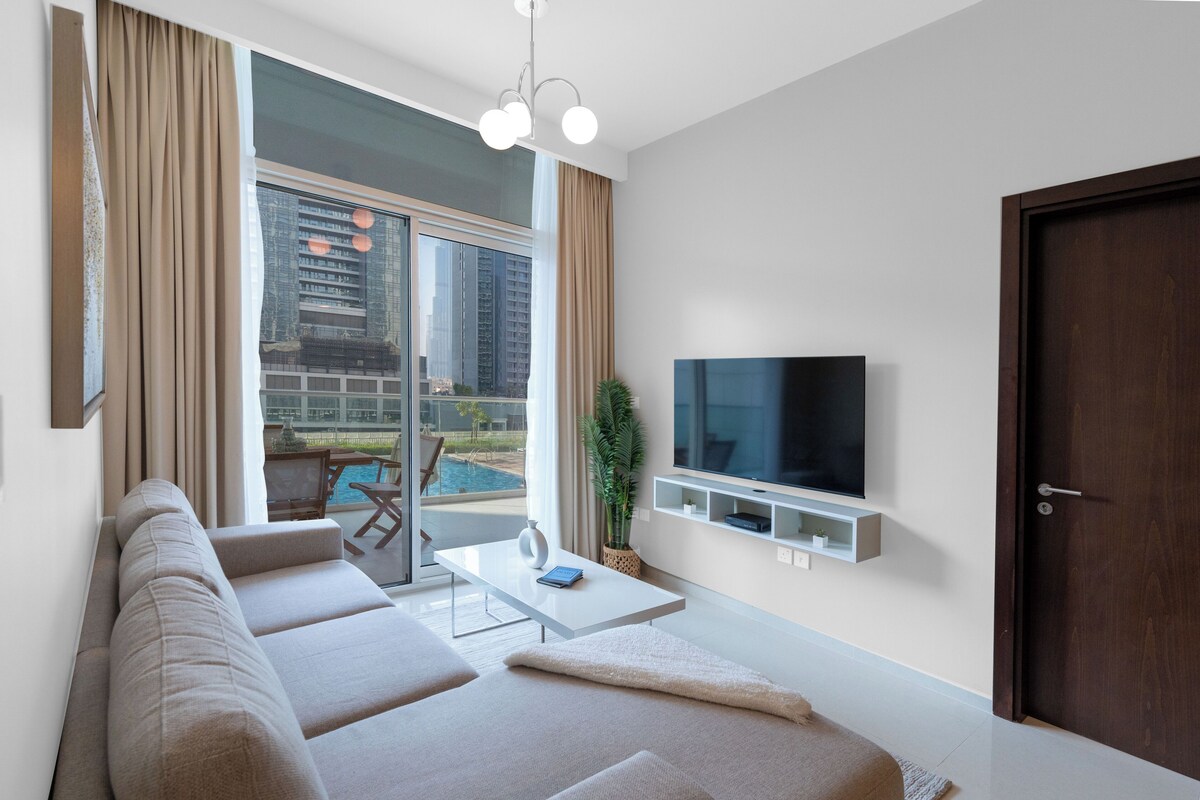 A modern living room with a sofa, TV, and a view of a swimming pool.