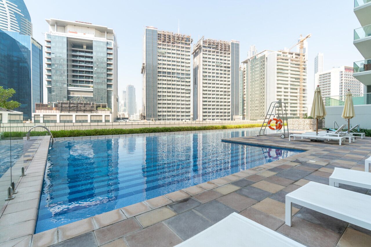 A rooftop pool with a cityscape view, white lounge chairs, and a lifebuoy.