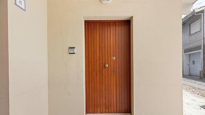 Een houten deur met een handgreep en een sleutelgat, in een beige muur, met een klein lampje erboven.
