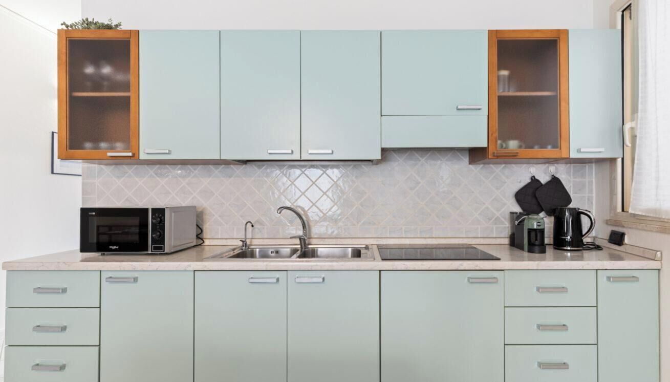 A kitchen with light green cabinets, a double sink, a microwave, a kettle, and a coffee maker.