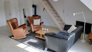 Een moderne woonkamer met een bank, twee fauteuils, een salontafel en een televisie.