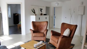 Een woonkamer met twee bruine leren fauteuils, een houten bijzettafeltje met drie witte kaarsen, en een witte kast met wanddecoratie.
