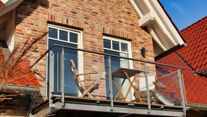 Een gebouw van baksteen met een balkon, een raam en een rood dak.