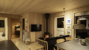 Ein gemütliches Blockhauss-Interieur mit Essbereich, Wohnzimmer mit Sofa, Fernseher und Kamin.