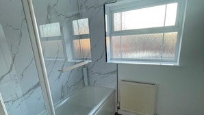 Ein Badezimmer mit einer Badewanne, einem Fenster und einer Heizung.