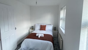 Ein Schlafzimmer mit Bett, Nachttischen, einem Heizkörper und einem Fenster mit Jalousien.