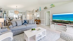 Un salon moderne avec un canapé, une table basse, un téléviseur et une cuisine en arrière-plan.