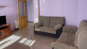 Ein Wohnzimmer mit einer Couch, einem Fernseher, einer Heizung und einer Tür.