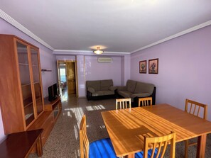 Une pièce comprenant une table à manger en bois, deux canapés, un buffet en bois et un téléviseur.