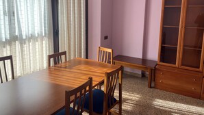 Ein Essbereich mit Holztisch und -stühlen, einer Bank, einem Schrank mit Glastüren und leichten Vorhängen an den Fenstern.