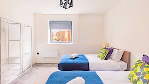 Ein Schlafzimmer mit zwei Betten, einem Fenster mit Jalousien, einem Heizkörper und einer Pendelleuchte.