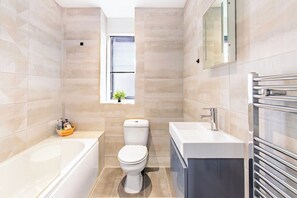 A modern bathroom with a bathtub, toilet, and vanity. - Modern City Centre Flat (Norwich)