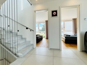 Ein modernes Interieur mit einer Treppe, einer Tür mit Rauchverbotsschild und einem Blick in ein Schlafzimmer mit Bett und Vorhängen.