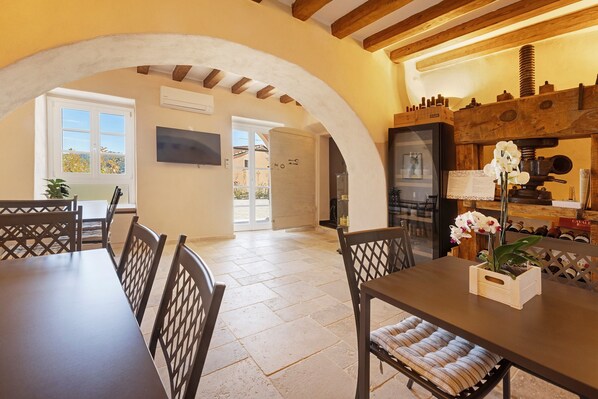 A dining area with a table and chairs, a wooden ceiling, and a kitchen area with a wine rack.