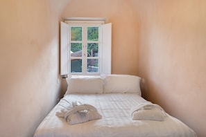 Una habitación pequeña con cama individual, ventana, paredes blancas y vista a zonas verdes.