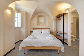 A bedroom with a bed, a window, a door, and a bathroom visible through an archway.