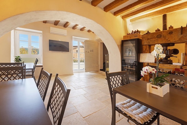 A dining area with a table and chairs, a wooden ceiling, and a kitchen area with a wine rack.