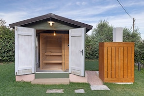 A small wooden structure with an open door, a light fixture above the door, and a chimney on the roof. - Room 'Timo' with Shared Garden, Wi-Fi and Air Conditioning (Olle-Viotti)