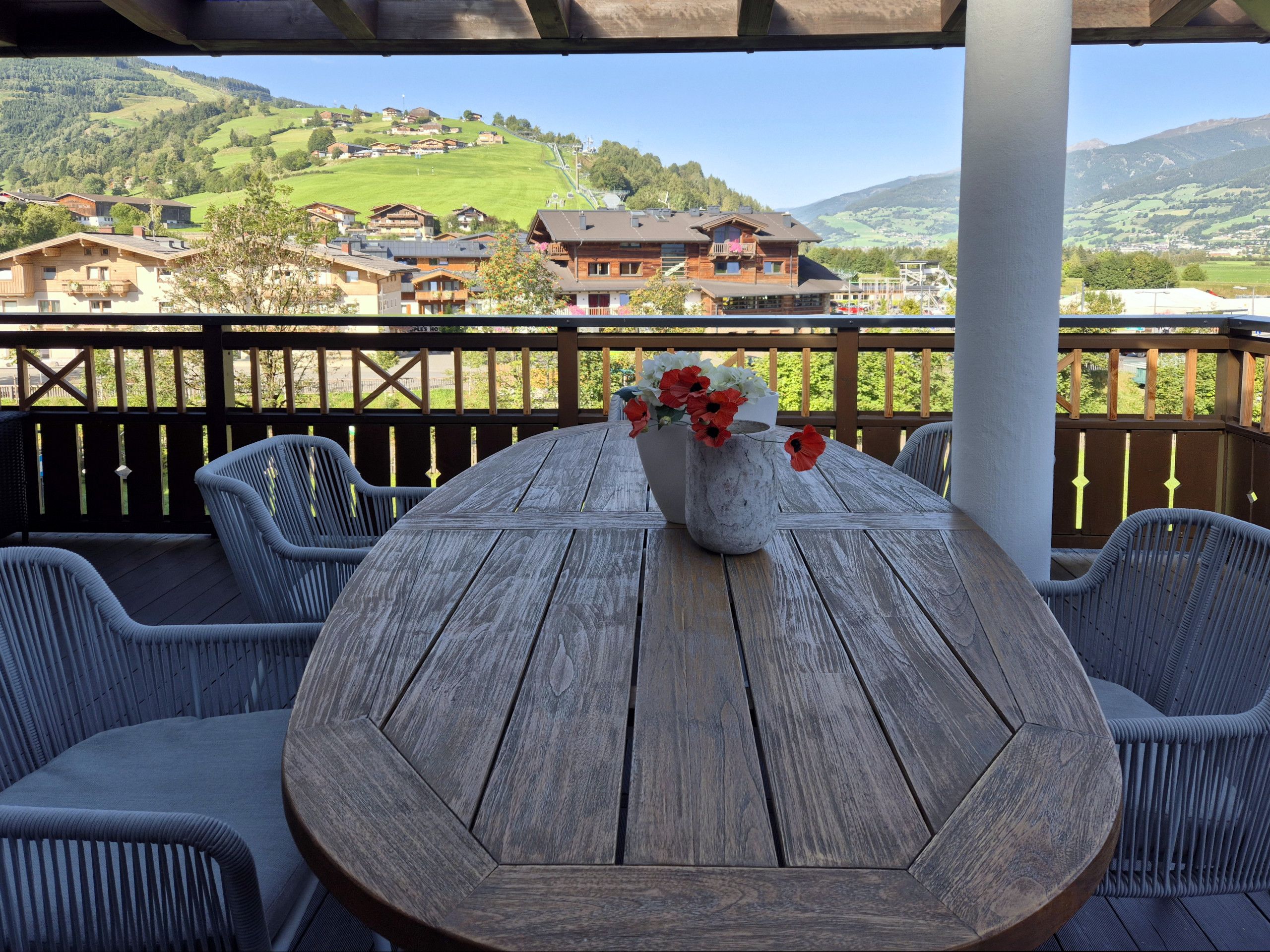 Ein Holztisch mit einer Blumenvase auf einem Balkon mit Blick auf eine gebirgige Landschaft.