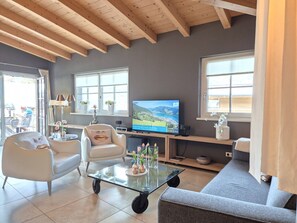 Ein Wohnzimmer mit Fernseher, Sitzgelegenheiten und Blick ins Freie.