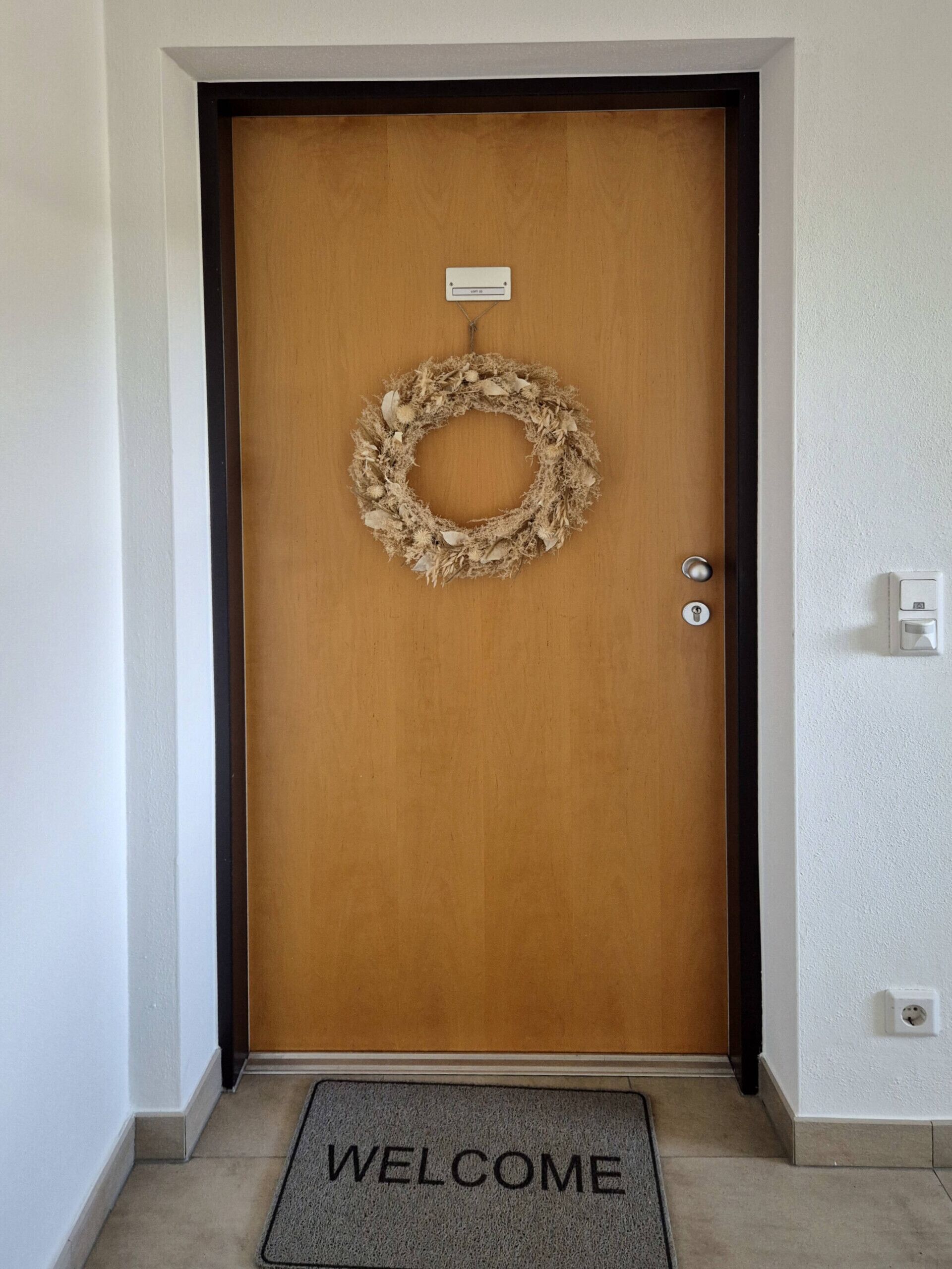 A wooden door with a wreath, a welcome mat, and a keyhole.