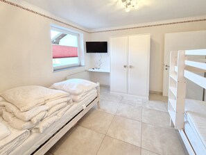 Un dormitorio con cama, armario, televisor y ventana con persianas.