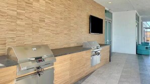Zona de recepción con pared de madera, televisor de pantalla plana y mostrador con dos parrillas empotradas.
