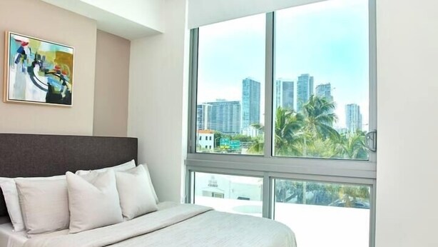Habitación de hotel con una cama grande, vistas a la ciudad y un cuadro en la pared.