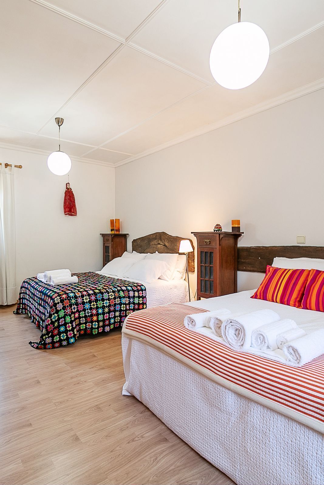 Una habitación de hotel con dos camas, un cabecero de madera, una colcha a rayas blancas y rojas y otra colcha con estampado floral.