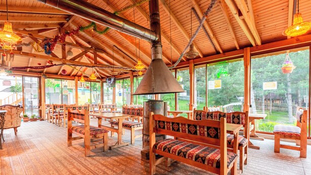 A wooden interior with benches and tables, large windows, and a chimney.