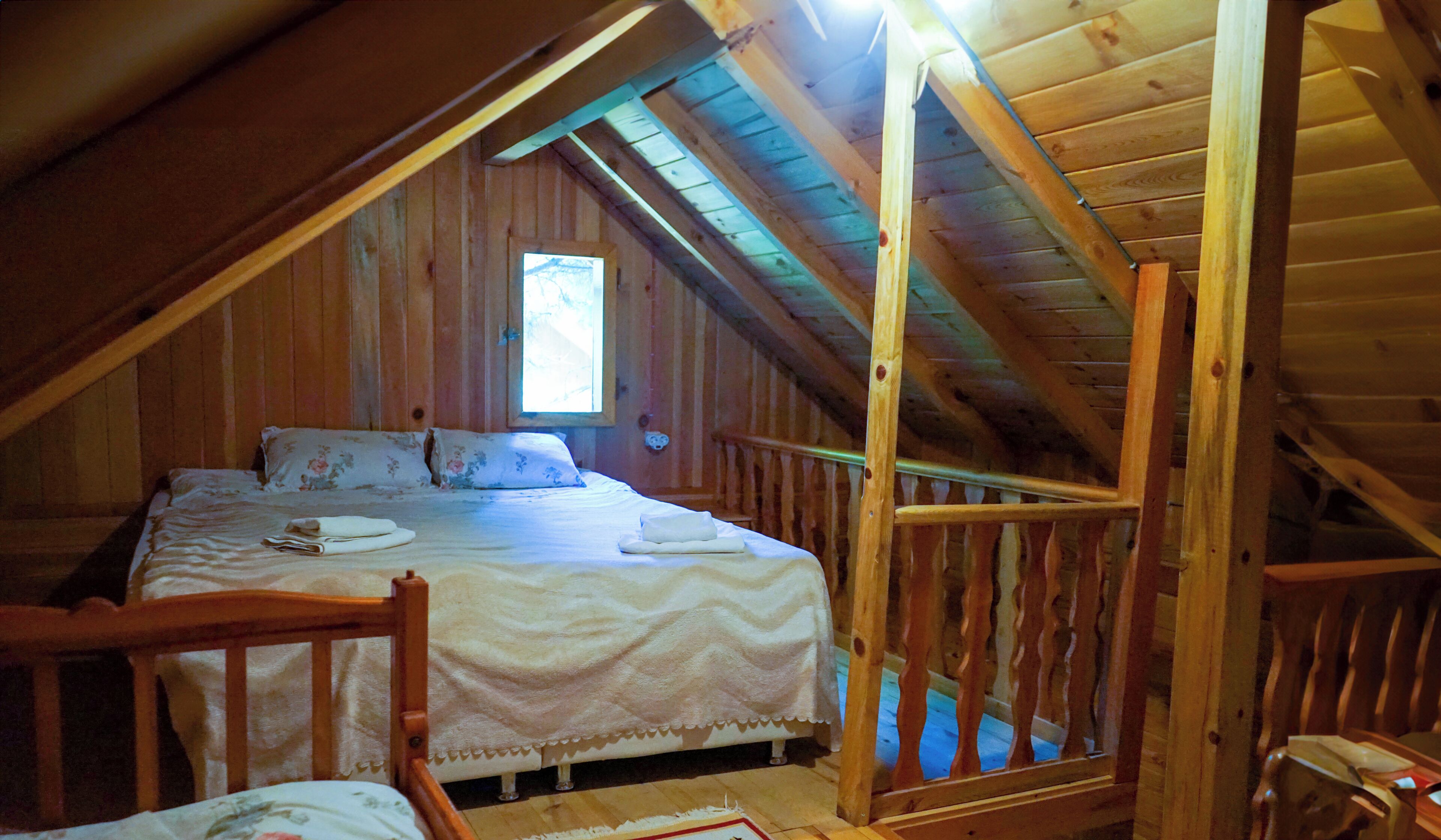 A wooden attic bedroom with a bed, a window, and a wooden railing.