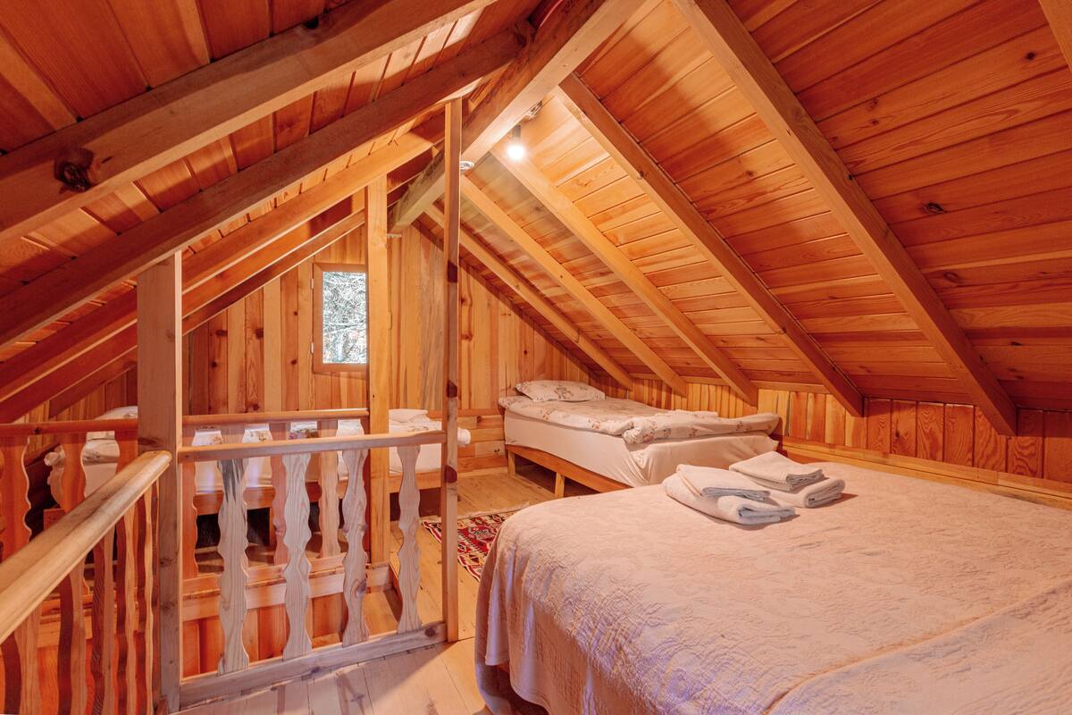 An attic bedroom with wooden beams, a loft-style bed, and a small window.