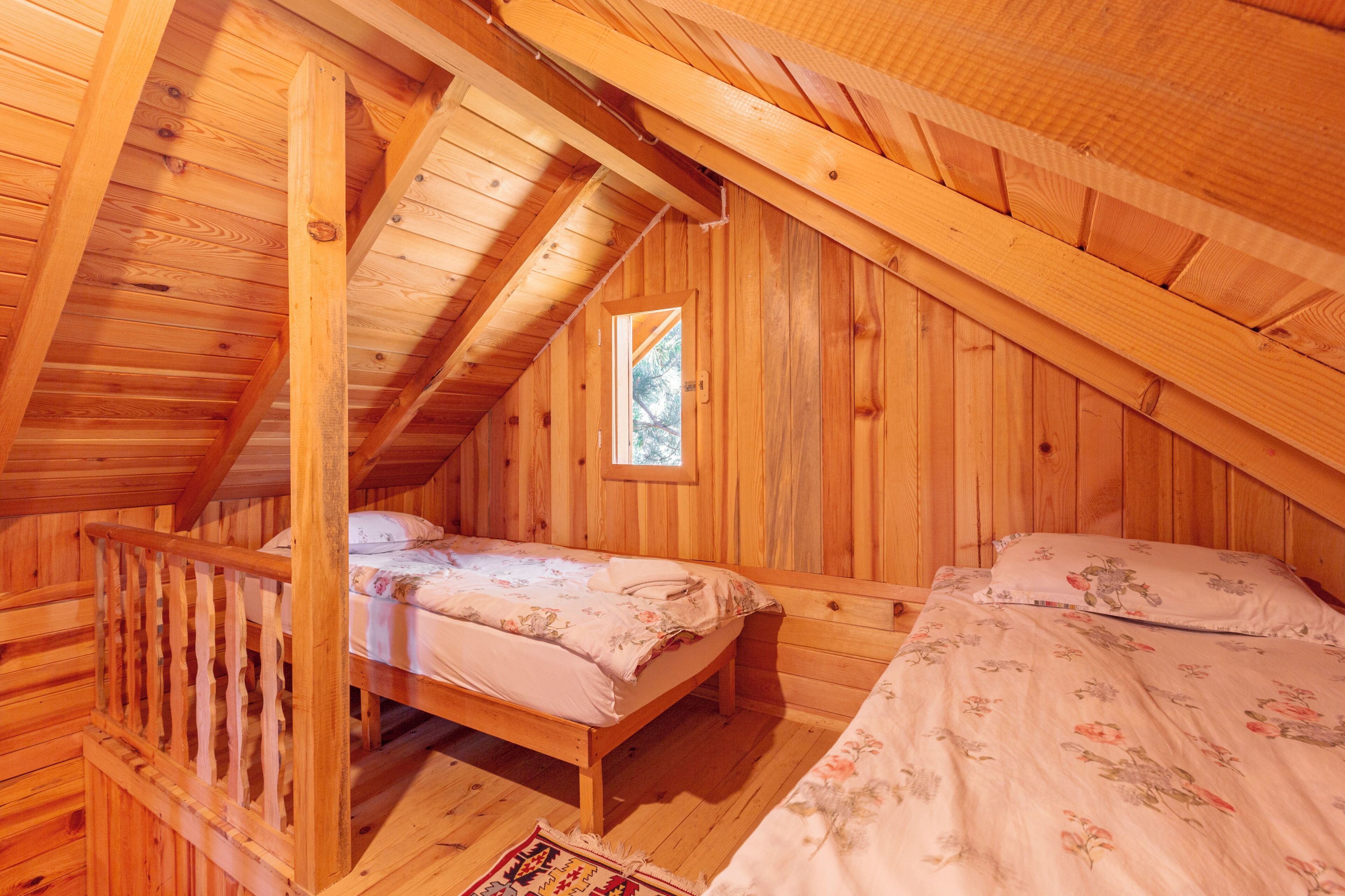 A wooden cabin with a loft bedroom, a small window, and a wooden staircase.