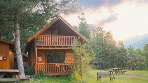 A wooden cabin with a balcony, a picnic table, and a bench.